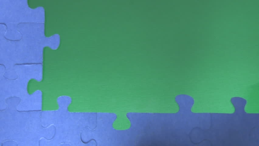Part of the blue completed puzzle on the green background. Hand is bringing missing parts and placing them into the correct place