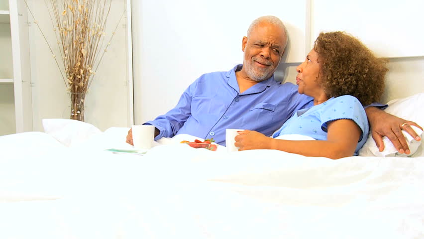 Elderly ethnic heterosexual couple enjoying eating breakfast bedroom home