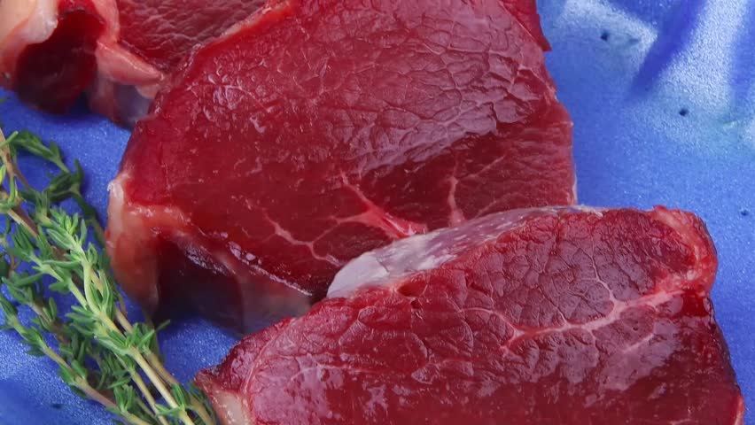 fresh raw beef fillet medallions with thyme twig on blue tray isolated over white background