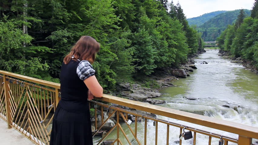 nice woman stands near railing bridge and looks on waterfall in Carpathian Mountains