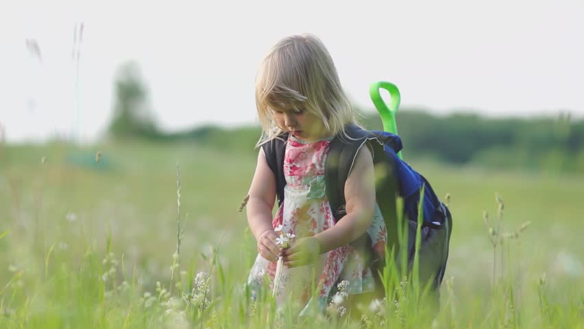 Adorable girl with huge backpack and toy shovel walking in park