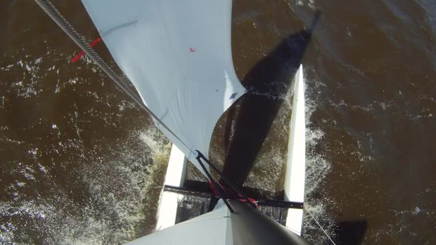 Catamaran cutting through the waves, sailing downwind over port, seen from the top of the mast