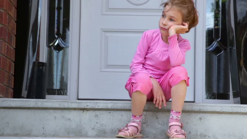 Little girl is bored when sits on porch near door of cottage