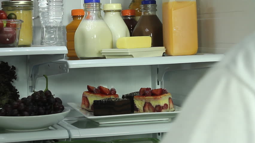 Man opens refrigerator, reaches for plate of strawberry, chocolate cakes, chooses to eat unhealthy food choices. 1080p