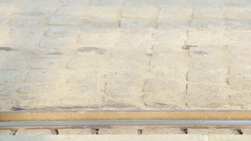 A blue low-floor tram is arriving to a station, focused on itâs rusty wheels