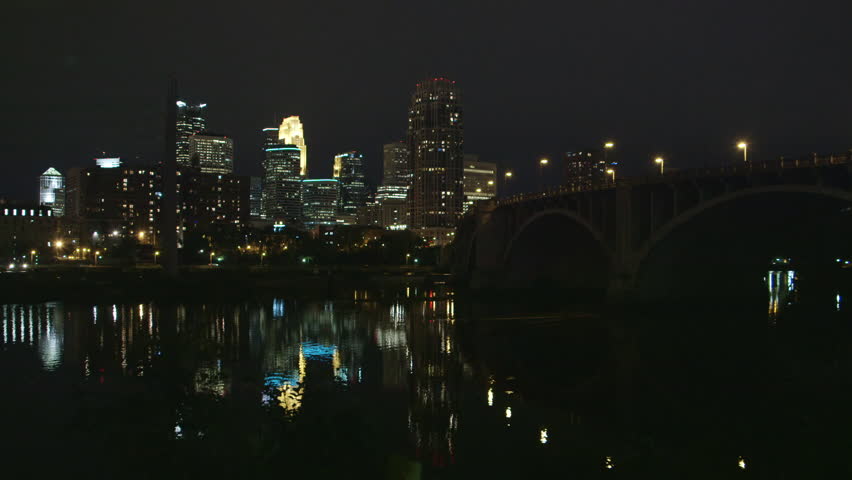 Two clips showing two views of the downtown Minneapolis night skyline, with the Mississippi River in the foreground.