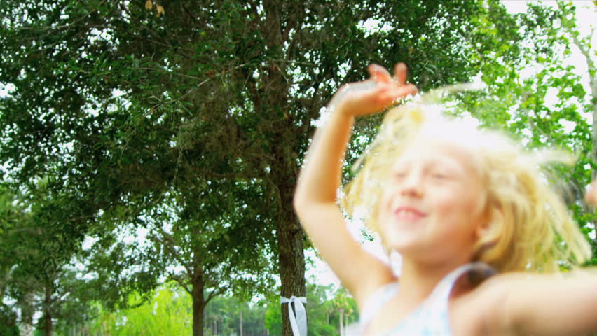 Cute little blonde girl jumping for joy in sunshine in home garden