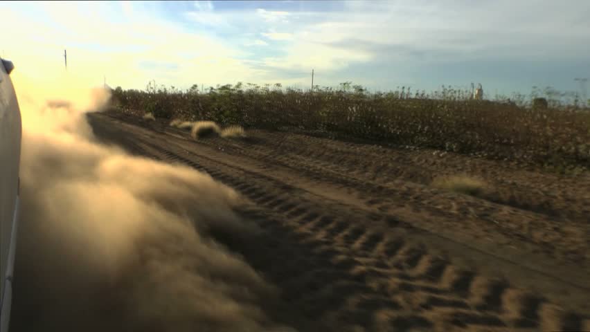 Car drives along dry, dirt road, its spinning wheels kick up mini dust storm. 1080p