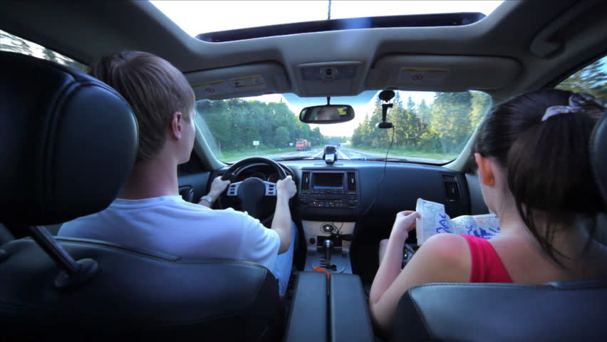 guy in white vest drives car and nearby girl solves Japanese crossword puzzle