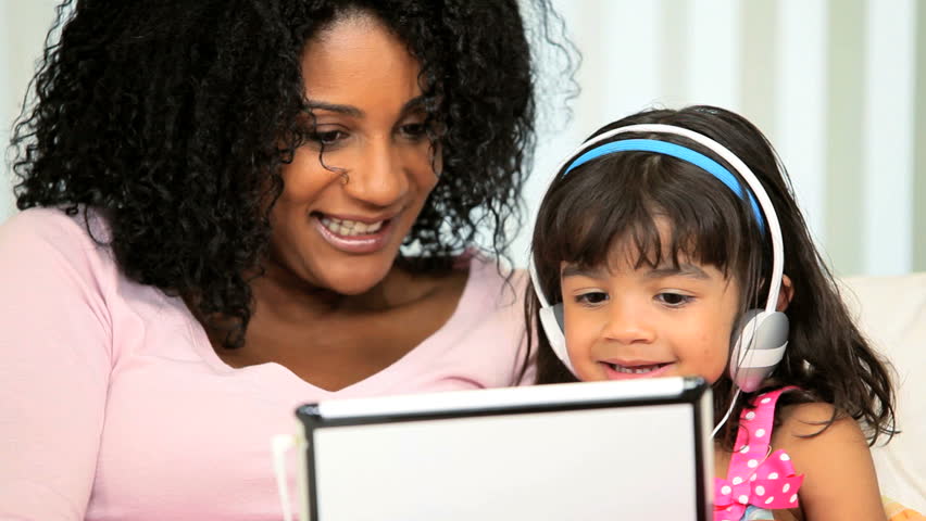 Loving African American mother with cute young daughter playing games wireless tablet