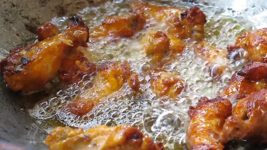 Chicken drummets deep frying in oil in a cast iron frying pan
