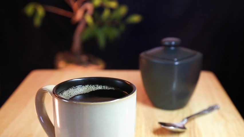 Pouring steaming hot coffee into a mug then stirring in some sugar.