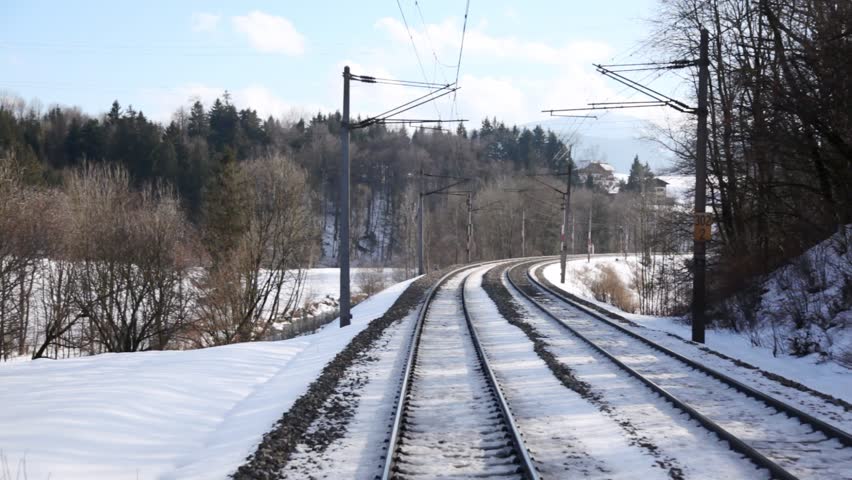 Train goes by rail near with inhabited locality along electric mains in sunny weather