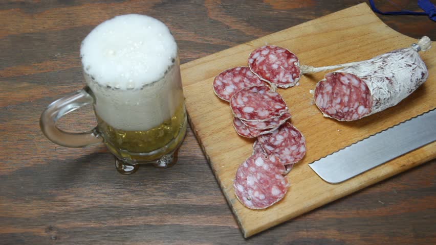 pouring beer in a glass,  salami and  knife on wooden cutting board
