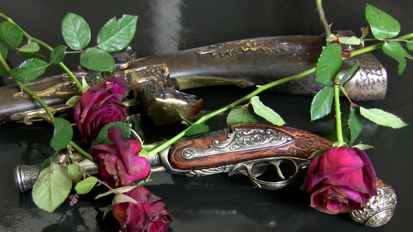 Close up of two retro guns on the dark grey background with withered red roses falling on them