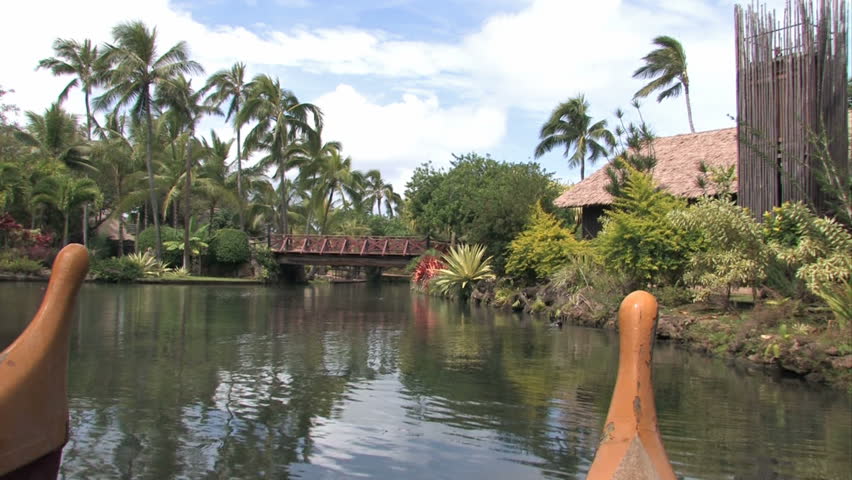 Polynesian canoes in a tropical pool in Oahu, Hawaii. Twin hull. Palm trees and tropical huts. Polynesian Cultural Center, Hawaii number one tourist attraction. Show the various islands of Polynesia. 