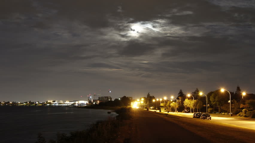 2 shots Time Lapse of Night Traffic both on the ground and in the air. Plane Landing in a cloudy night. And cloudy moonlight night, busy ground traffic with Richmond Olympic Oval in a distance