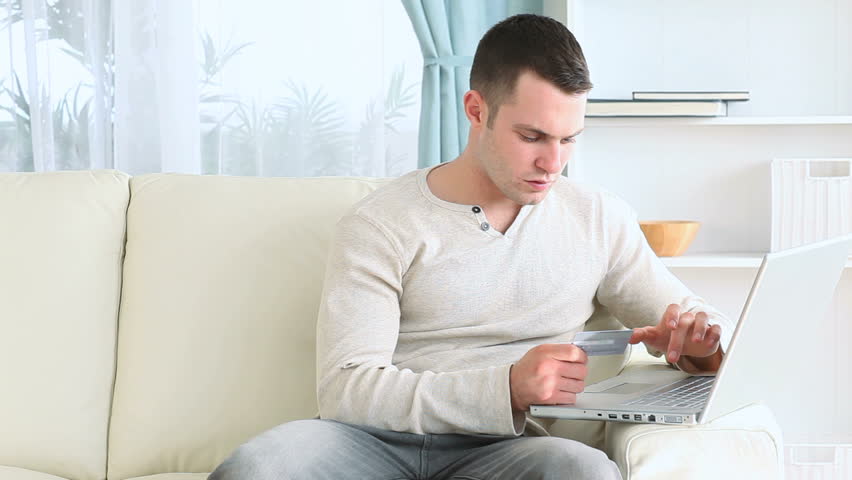 Young man using his payment card online in his living -room