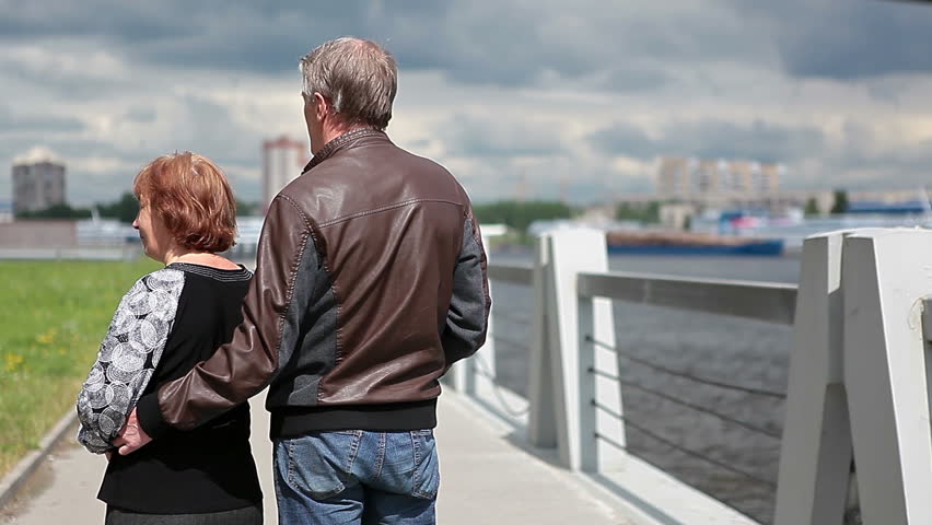 Senior happy couple standing on embankment, turning, waving and going forward to the distance
