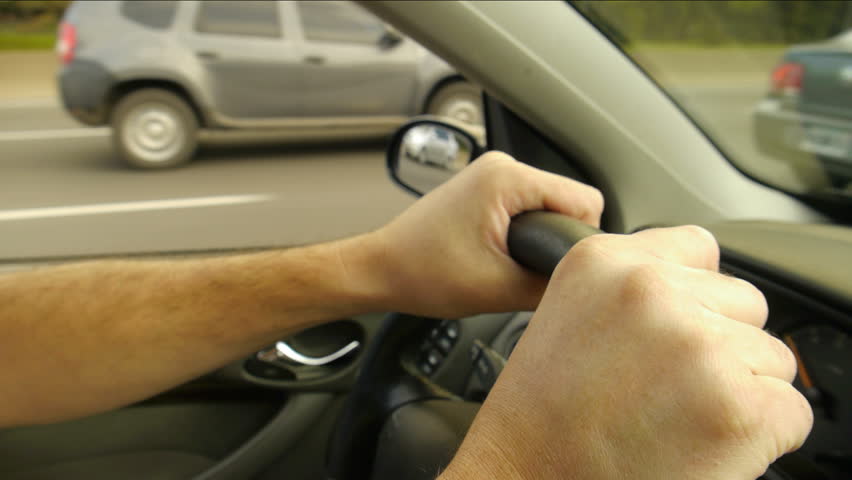 Driving a car on the freeway. Male hands and on steering wheel. close Up.