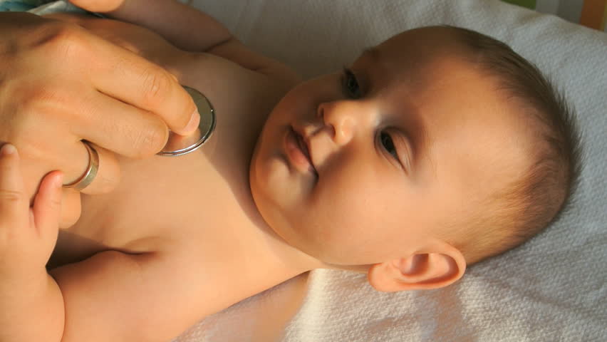 Cute baby is lying on his back and smiling. A male doctor examining babyâs chest for heart beat with a stethoscope.