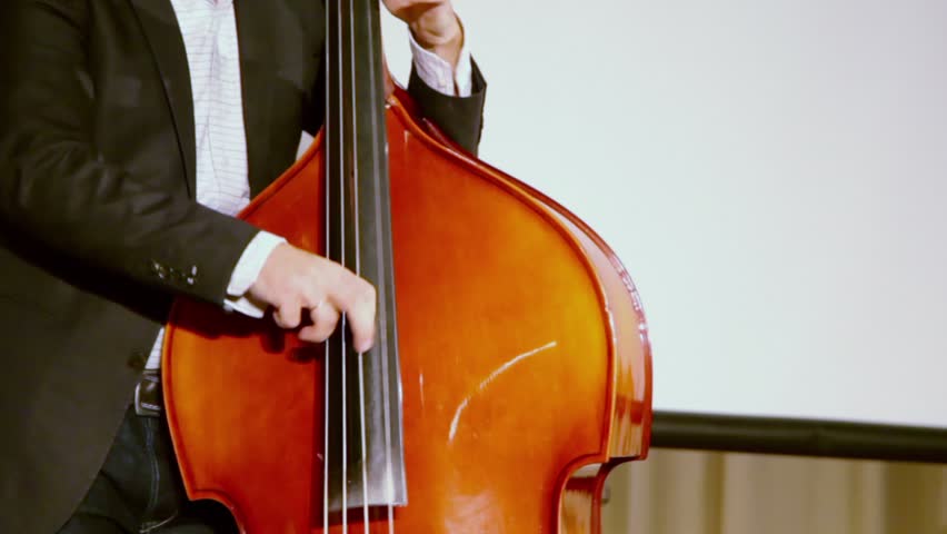 Man plays on contrabass on stage near screen and curtain during concert