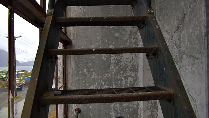 Climbing up the outer fire escape stairs of the spooky old Buckner Building in Whittier, Alaska and looking in through broken window to a room of decay, ruin, and graffiti.