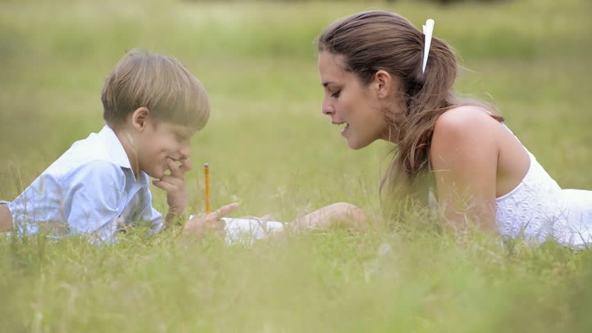People and education, mother helping child with homework, lying on grass and reading book at park. Medium and wide shot in sequence