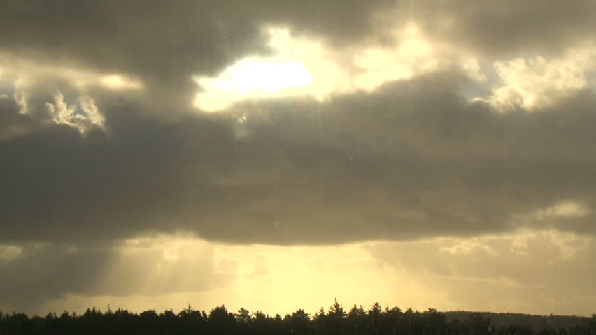 Sunlight shining through heavy rain cloud over trees at sunrise, time lapse.