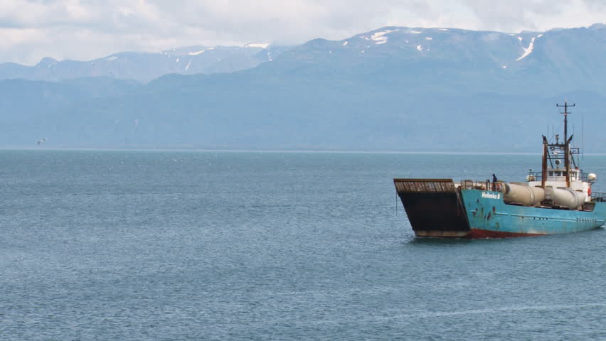 HOMER, AK - CIRCA 2012: A weatherworn landing craft on approach to the harbor with its cargo of a diesel tractor truck and four tank trailers. The bow gate is opening.