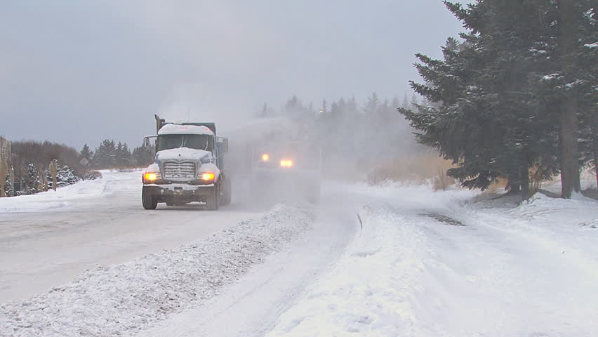HOMER, AK CIRCA 2012: Snow blower on an excavator paired with a dump truck to clean plow piles on snowy city street.