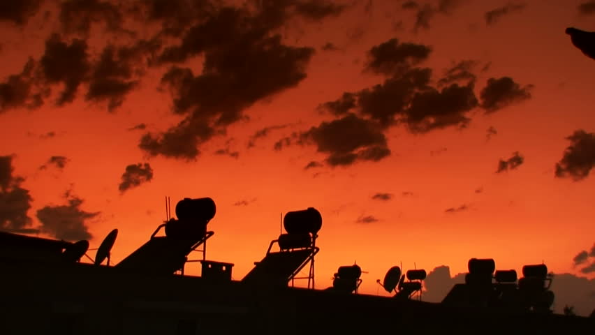 Time-lapse clouds over silhouetted holiday villas with solar heating panels on the roof