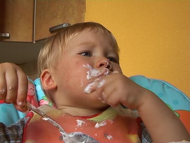 Baby learning to feed himself with a spoon and getting messy in the process