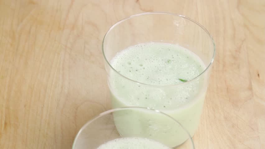 A cucumber and yogurt drink being garnished with mint leaves