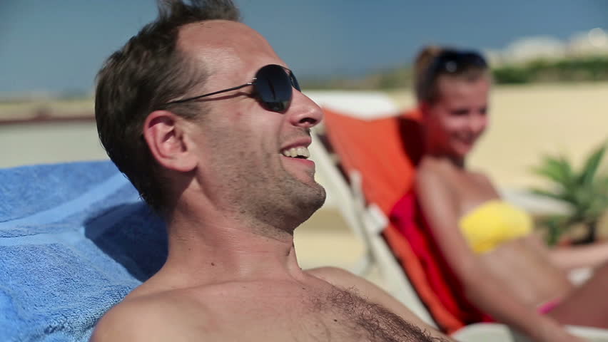 Happy couple chatting and sunbathing on sunbeds
