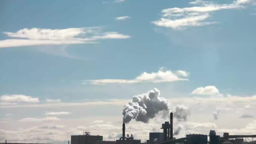 Pollution emits from distant stack and fills blue sky with various chemicals that contribute to air pollutants overall.