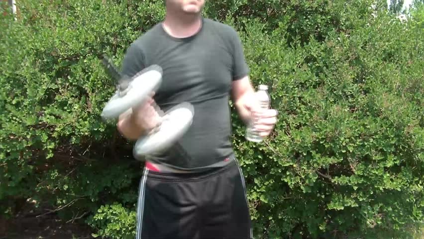 Man sweats in sun and performs bicep curls exercise with dumbbell weight while holding bottle of water in other hand.