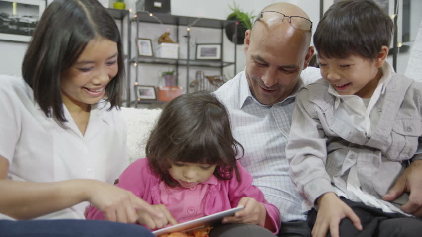 A happy family of Asian ethnicity are spending time together at home. They are all gathered round a digital tablet. In slow motion