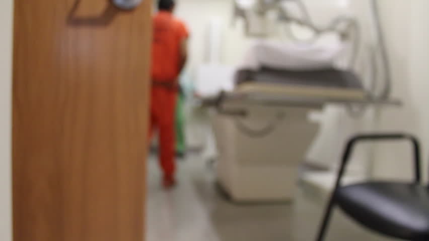 An out of focus video of a real inmate in an orange jumpsuit being xrayed