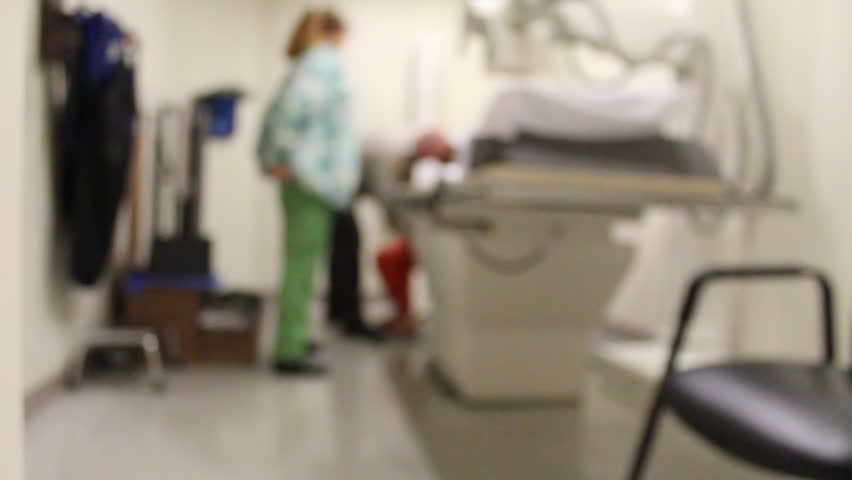 An out of focus video of a real inmate in an orange jumpsuit being xrayed