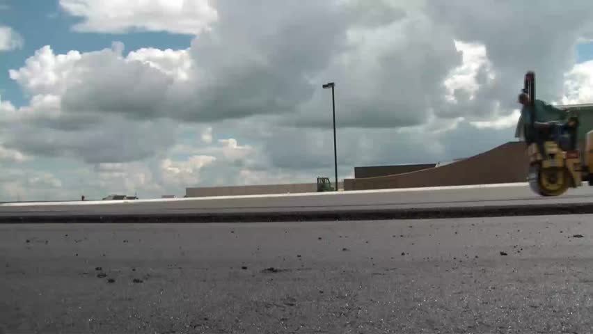 Clip of man driving in reverse with blacktop pave rolling machine to smooth or flatten out newly laid tar material.