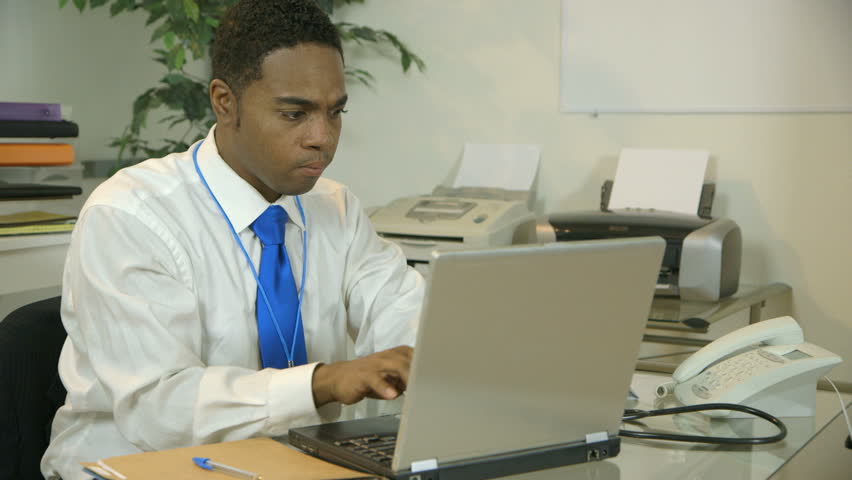A fatigued young African American doctor sits down at his desk after a long day.