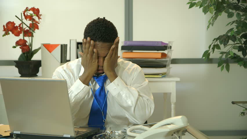 A doctor or surgeon sitting in front of a laptop shows fatigue as he removes his stethoscope and cap as if calling it a day.