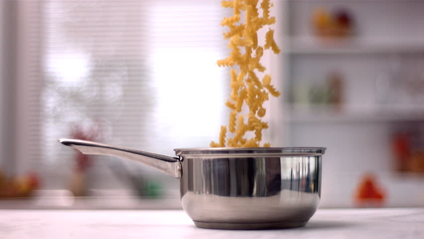 Fusilli falling in saucepan in kitchen in slow motion
