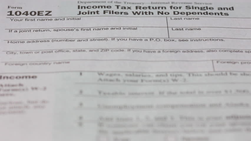 Rack focus and tilt shot of 1040 annual tax return form and and hundred dollar bills falling onto it close up
