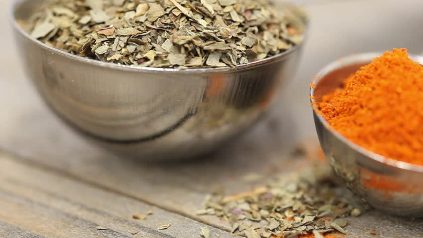 Various mixed spices (oregano, curcuma, paprika, anise) in metal scoops on wooden table