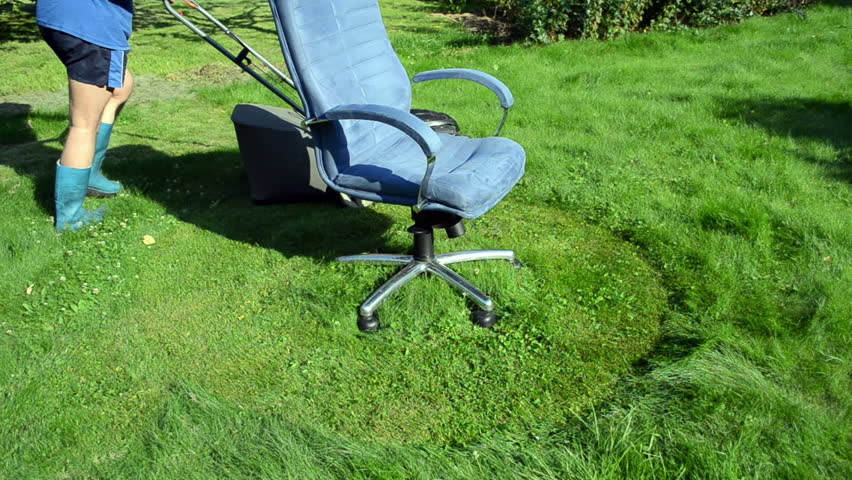 concept of man with shorts and rubber boots cut lawn grass with cutter mower arround office boss chair.