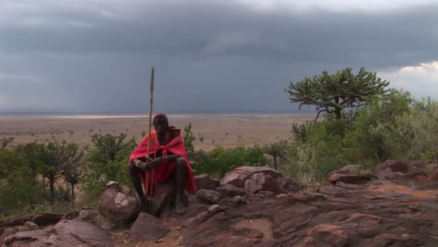 Masai Warrior in traditional clothes sitting and singing before the Storm.