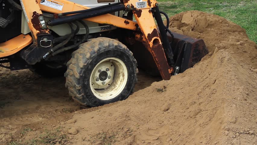 Front end loader moves a pile of dirt near a recently constructed backyard stone patio. Shot in 1920x1080p HD widescreen.