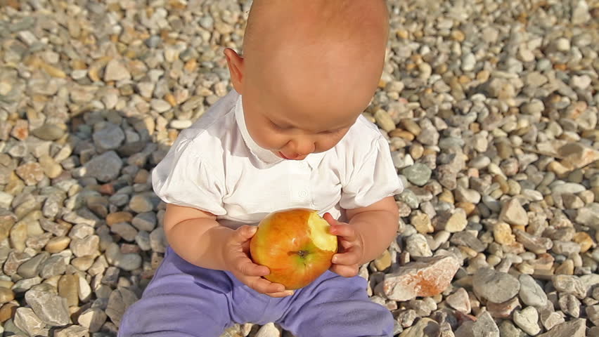 Baby playing and eating an apple on pebbles background.